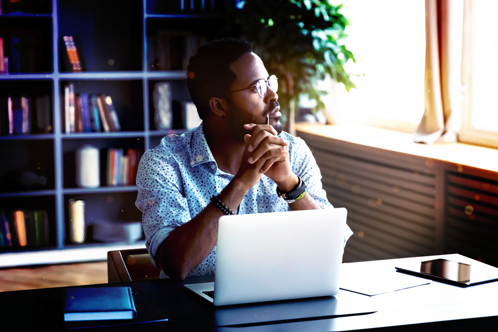 man sitting at laptop looking out the window thinking